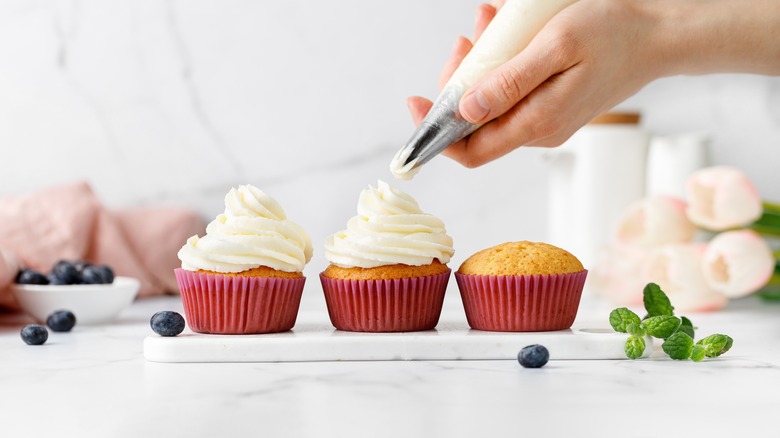 whipped cream being piped onto cupcakes