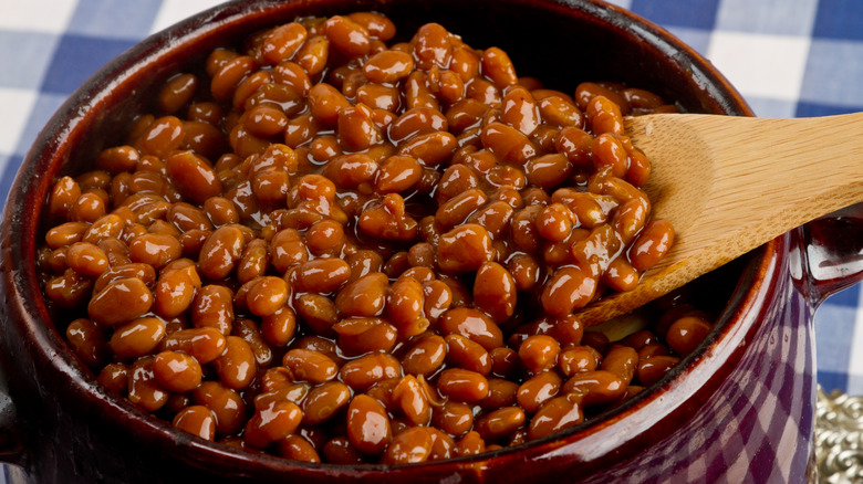 Baked beans in pot being scooped with wooden spoon