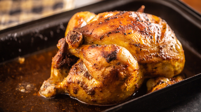 Full roasted chicken basting in juices in a pan