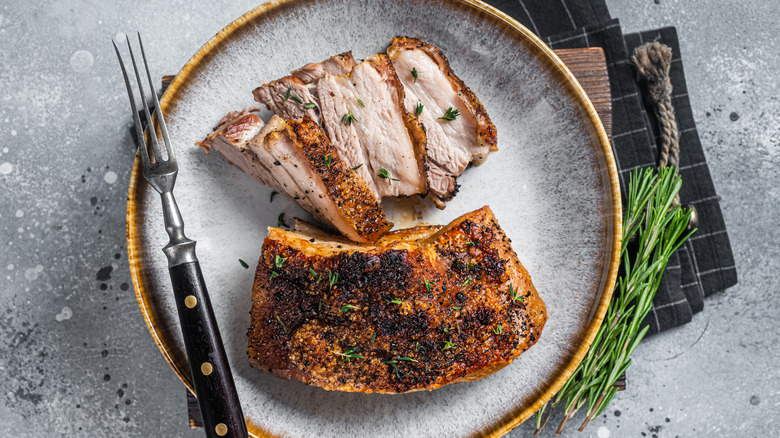 Pork belly on a plate  with herbs on the side.