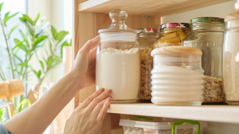 Hands set a glass jar of flour on a pantry shelf