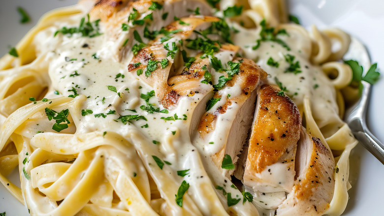 A serving of creamy chicken Alfredo pasta with garnish on a white plate