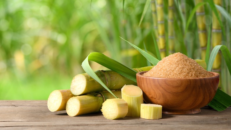 Crunchy turbinado sugar in a wooden bowl with sugar cane beside it