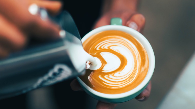 barista pours milk into cappuccino