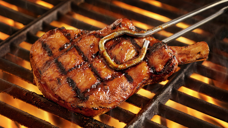 Pork chop held with tongs over hot grill