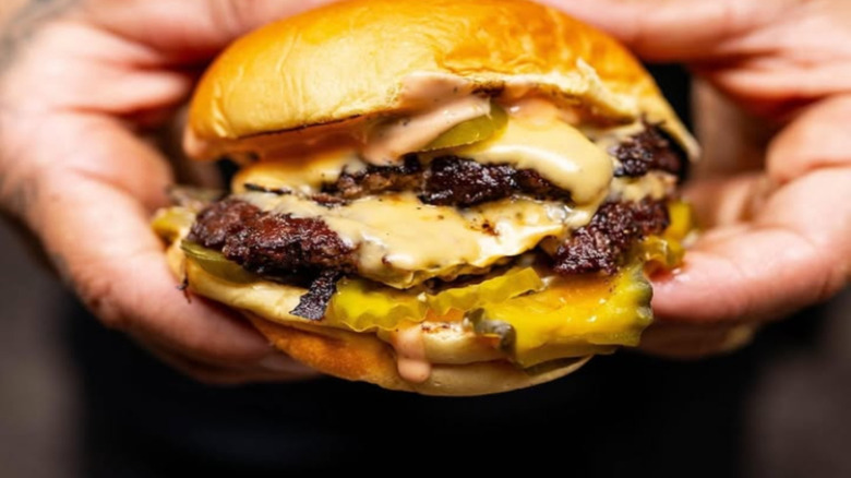 Double patty burger with cheese, sauce, and pickles being held in two hands