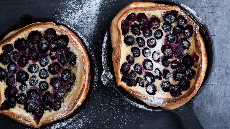 Two cast iron skillets holding blueberry Dutch baby pancakes are dusted with sugar