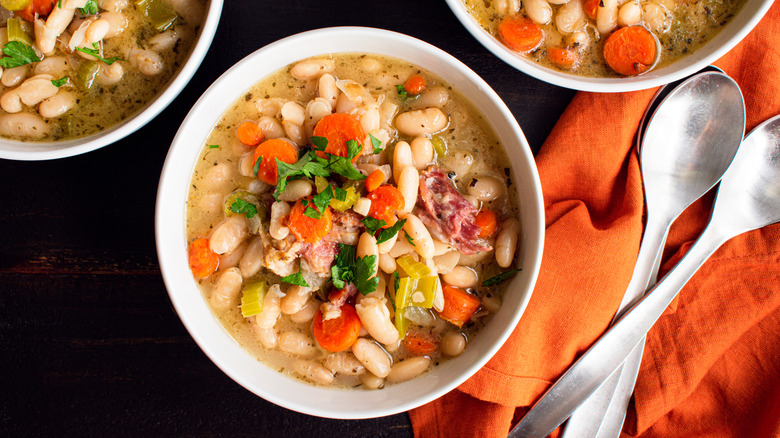 A white bowl of white bean soup with vegetables and fresh herbs