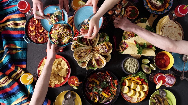 Variety of Mexican foods on table with people serving
