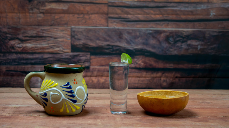 A shotglass of mezcal surrounded by a jicara and a clay pitcher