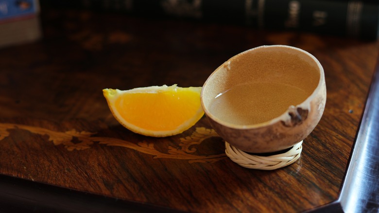 A copita filled with mezcal next to an orange slice on a wooden table