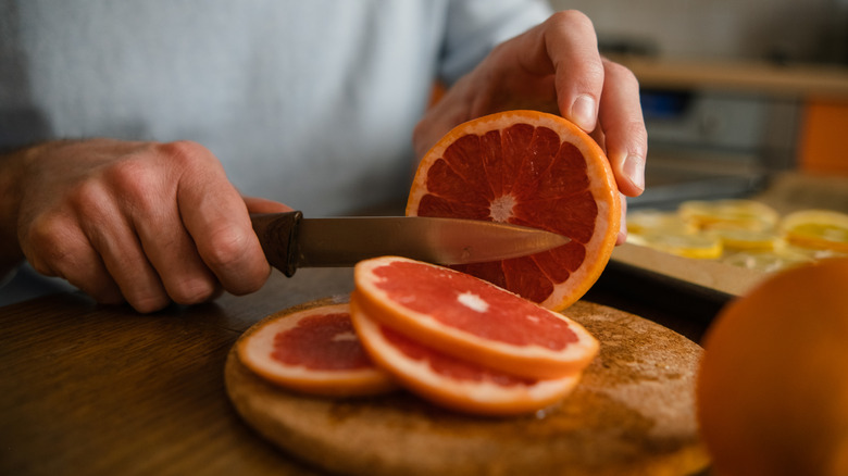 Hands cutting through a grapefruit on a wooden circular chopping board