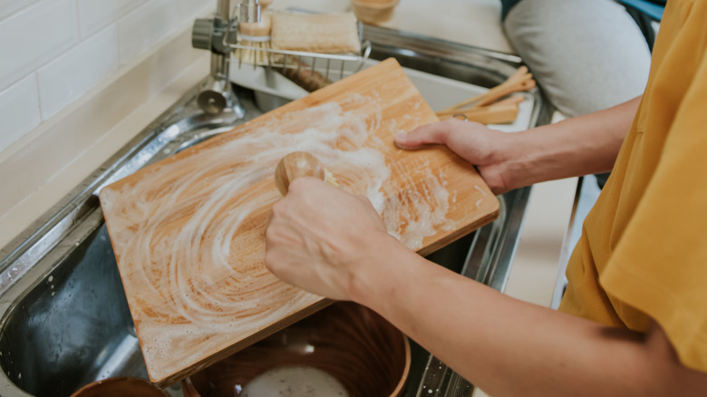 A person in a yellow shirt washes a wooden cutting board