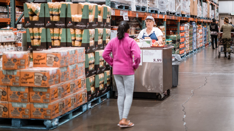 A Costco employee stands at a sample station while a customer approaches