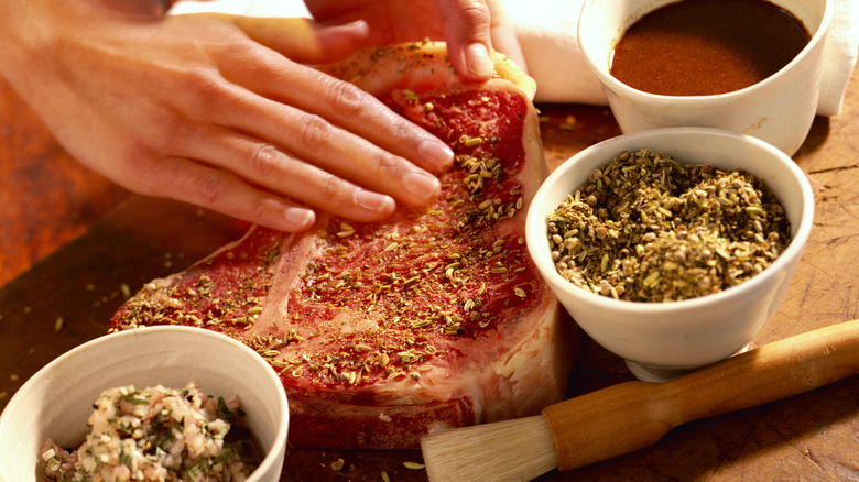 A hand presses a spice blend into a steak