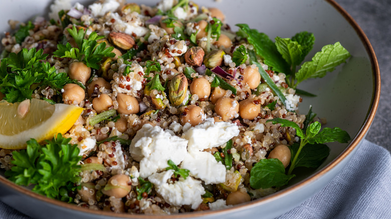 A colorful salad features a lemon wedge, fresh herbs, quinoa, pistachios, and chickpeas