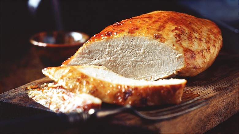 Sliced turkey breast on a wooden cutting board with a metal fork