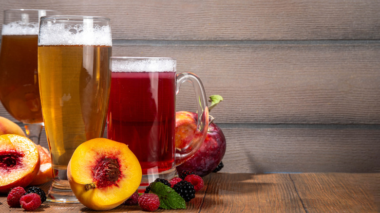 Three different beers sit surrounded by beautiful fresh fruits