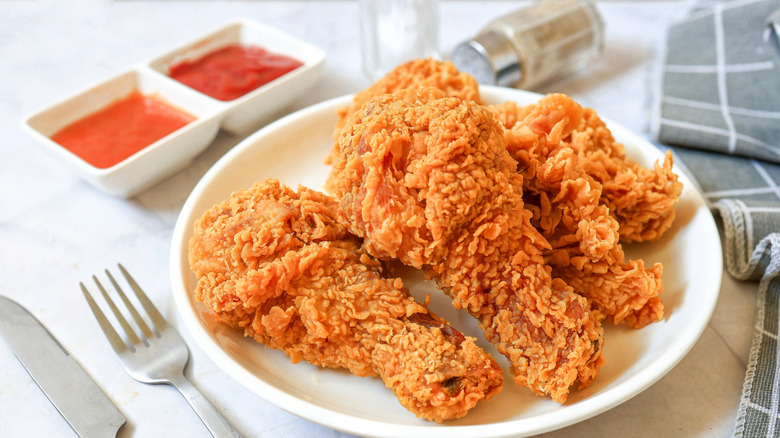 Crispy fried chicken drumsticks on a white plate with sauces on the side