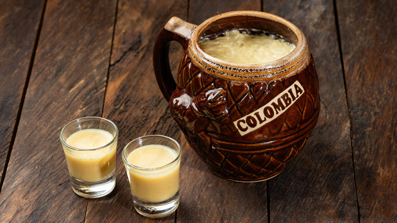 Two shot glasses of chicha next to a large mug with the word 