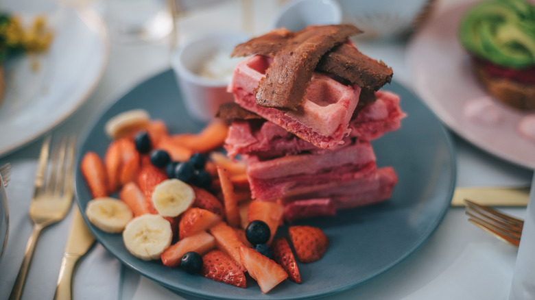 Vegan bacon slices sitting on top of pink waffles