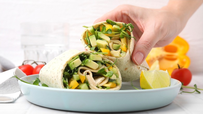 Hand holding half of a sandwich wrap filled with bell pepper and avocado slices