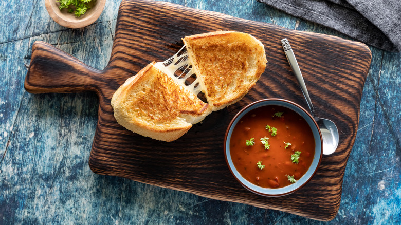 Grilled cheese and a bowl of tomato soup on a board