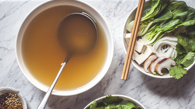 Broth in a bowl with a ladle next to a bowl of vegetables