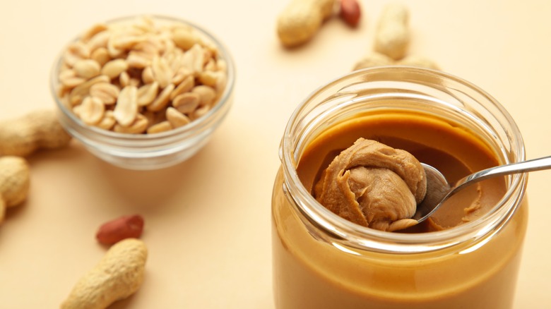 Jar of peanut butter with peanuts in background