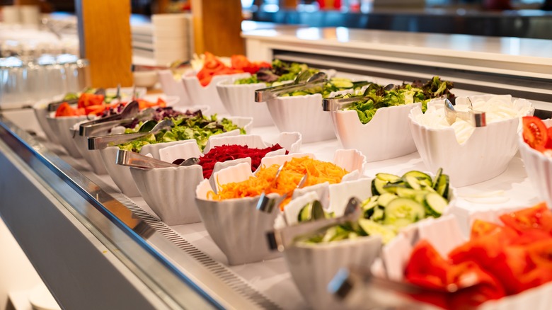 A salad bar at a restaurant with vegetables and toppings in white bowls