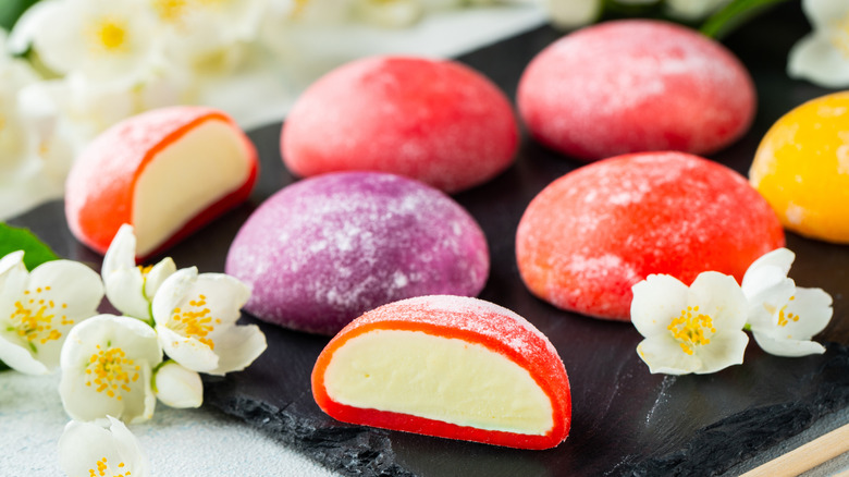 Red and purple mochi ice cream on black tray surrounded by flowers