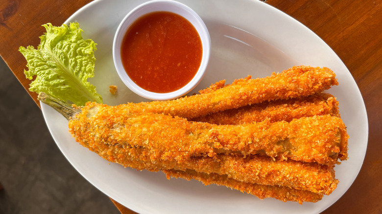 Top view of a plate of fried eggplant slices with a side of red dipping sauce, all sitting on the edge of a wooden table.