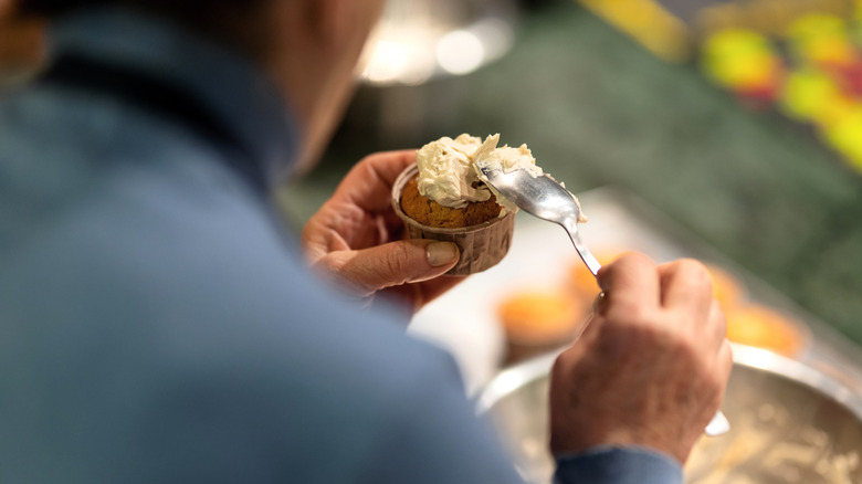 person spreading ermine frosting on a cupcake using the inside of a spoon