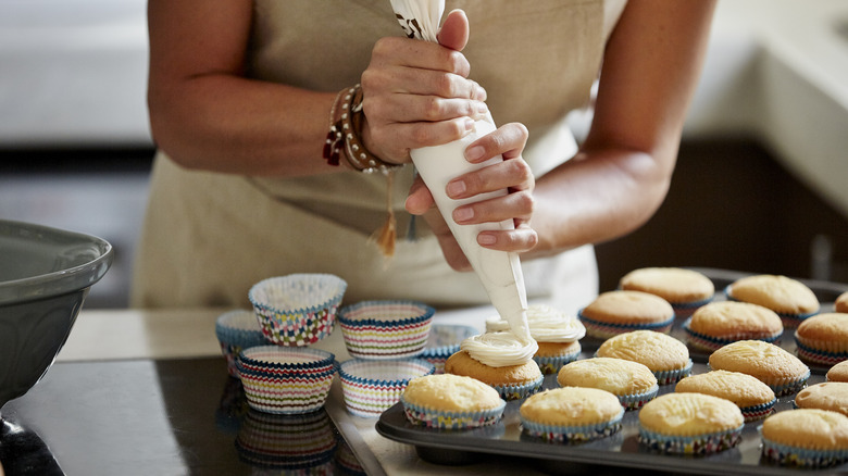 person in an apron piping a selection of cupcakes in a baking tray