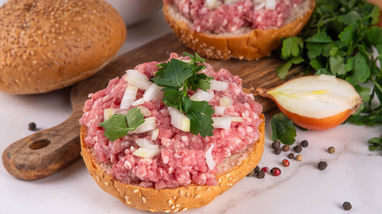 An open-faced raw beef sandwich staggered on a wooden board