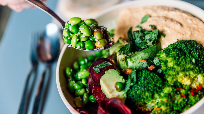 A spoon holds up a spoon full of edamame over a salad