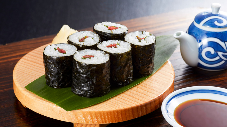 A plate of six ume shiso maki roll pieces next to a tea pot