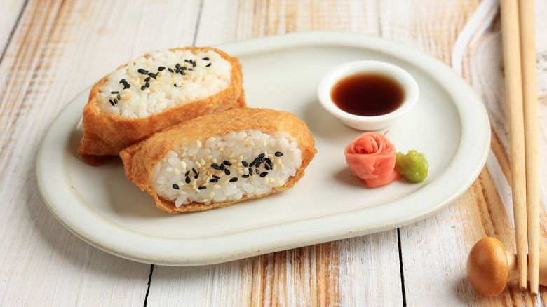 Two pieces of inarizushi next to soy sauce dish, pickled ginger, and wasabi