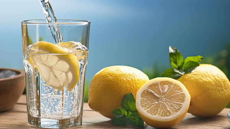 Water pouring into a glass with lemon slices next to lemons.