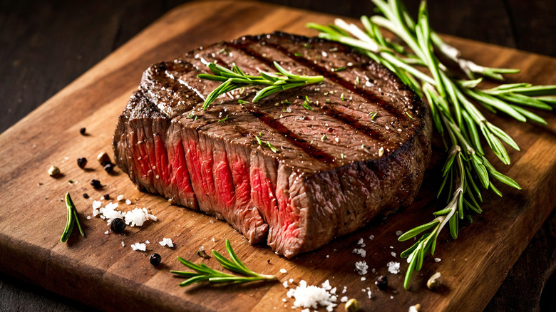 Grilled steak on cutting board with fresh herbs, salt, and pepper