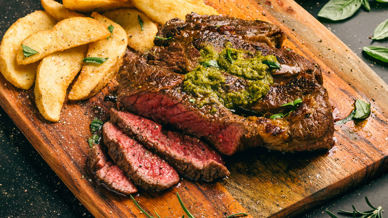 A steak covered in pesto next to steak fries