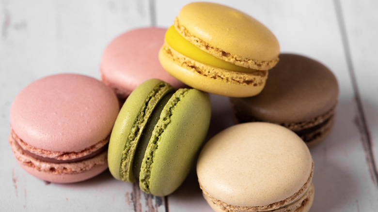 A stack of colorful macarons sits on a white wooden surface