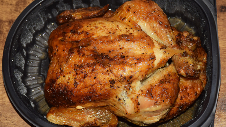 A tasty rotisserie chicken sits in a black plastic container