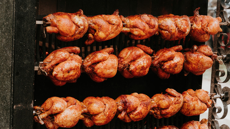 Lines of rotisserie chickens roast on open spits