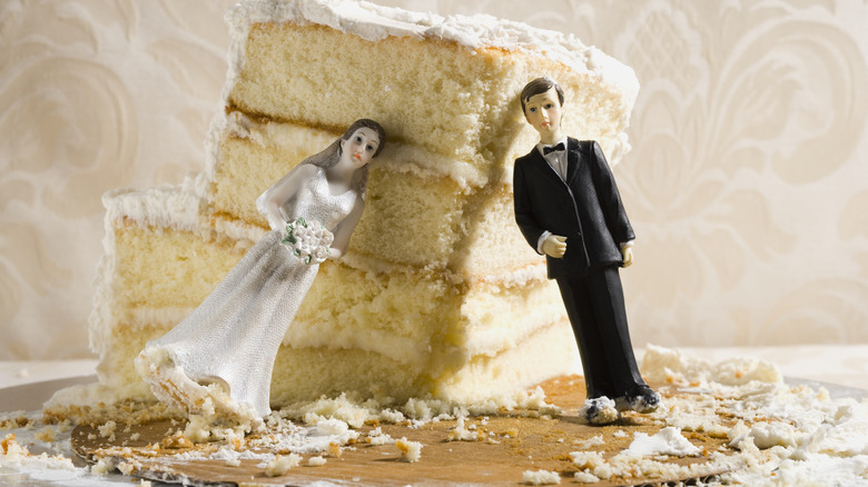 Bride and groom cake top figurines are propped against the remnants of a wedding cake