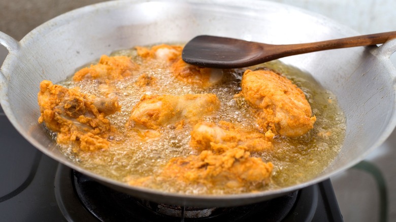 Fried chicken in pan of oil with wooden spoon