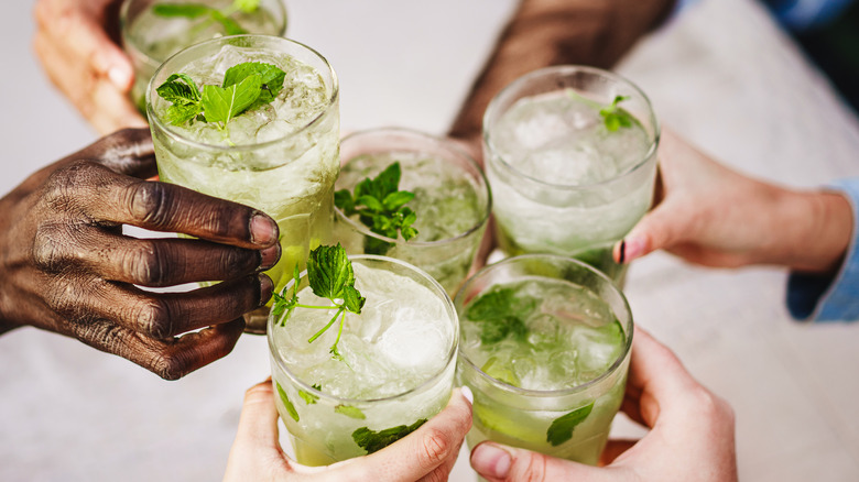 Hands holding mojito cocktails and clinking glasses