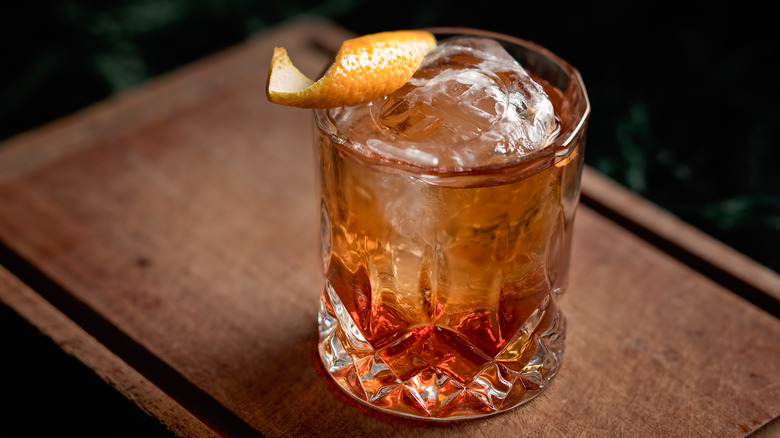 Old fashioned cocktail with orange twist on wood board