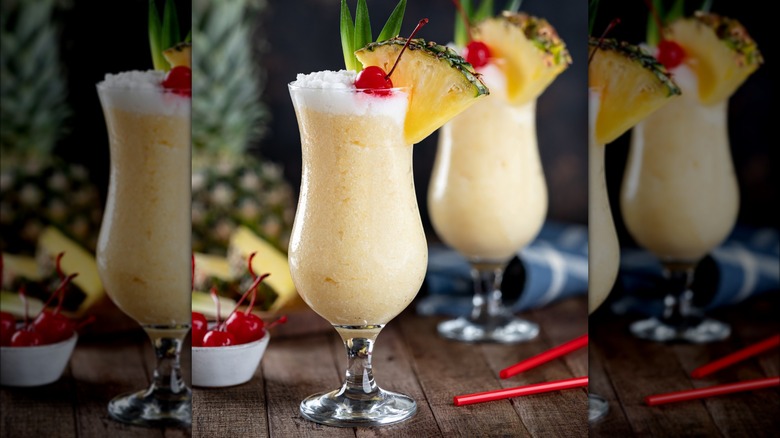 Pina colada cocktails on wooden table with bowl of red cocktail cherries