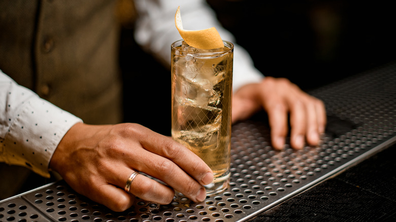 Bartender serves a whiskey highball with lemon twist